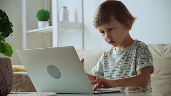 Child Using Laptop While Sitting on Sofa at Home Home Schooling Distance Learning
