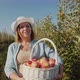 A Woman Farmer Carries a Basket with a Harvest of Apples Along an Apple Orchard - VideoHive Item for Sale