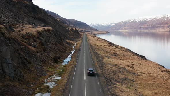 Drone Tracking Car Driving By Fjord And Towards Mountains