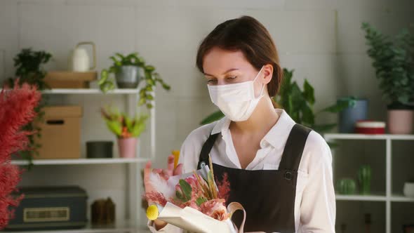 Young Florist Wearing Protective Mask Holding Wrapped Bouquet of Roses and Dried Flowers in