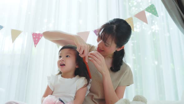 Asian loving mother spend leisure time combing young girl daughter's hairs in living room in house.