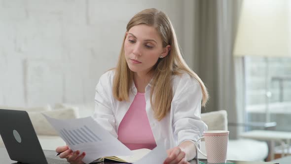 Focused Woman Sits at Home on the Desk and Works Using a Laptop Manager on a Remote Work During