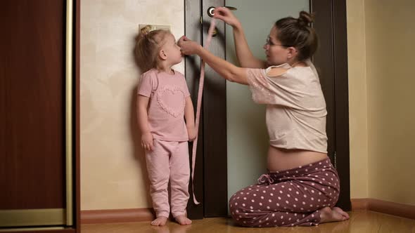 Young pregnant woman and mother measuring her daughter's height