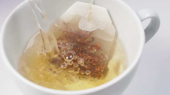 Pouring boiling water in a white cup with a bag of rooibos tea with fruit additives 