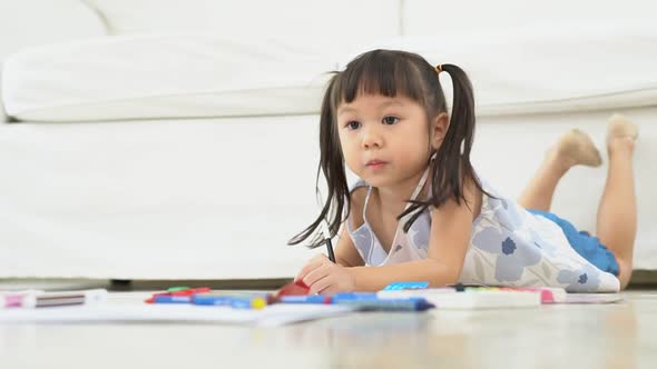 Cute adorable asian ethnic kid girl holding color pen drawing and painting, lying on warm floor, She alt