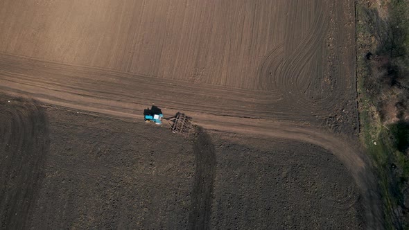 Top View of a Tractor with Harrow System Plowing Ground on Cultivated Farm Field