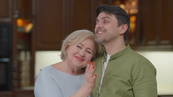 Happy Hugging Senior Mother and Adult Son Talking Smiling Standing at Home Indoors