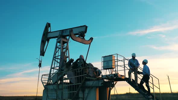 Male Engineers Are Standing on a Pumpjack and Observing the Site. Fossil Fuel, Crude Oil Concept
