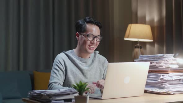 Asian Man Having Video Call On Laptop While Working With Documents At Home