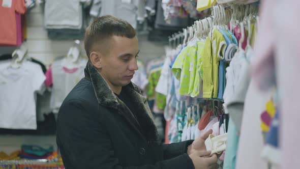 Handsome Man Looks at Children Clothing in Department Store