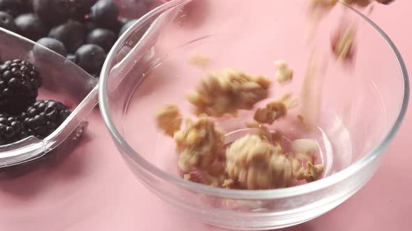 Falling Granola in a Glass Bowl with and Berries on Pink Background