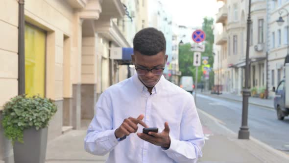 African Man Using Smartphone While Walking on the Street