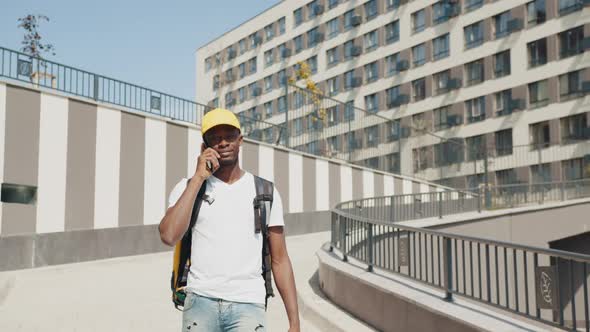 An AfricanAmerican Delivery Man with a Thermal Bag for Food Walks Down the