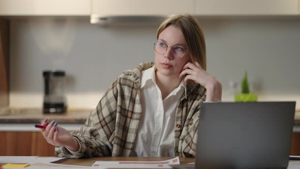 a Woman with Glasses Working on Financial Documents Sitting at Her Workplace Using a Laptop