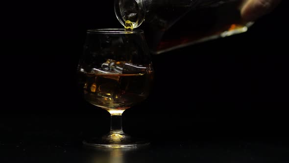 Pouring Whiskey, Cognac Into Glass. Black Background. Pour of Alcohol Drink