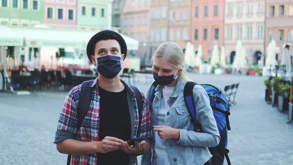 Young Tourists in Protective Masks and with Bags Using Smartphone