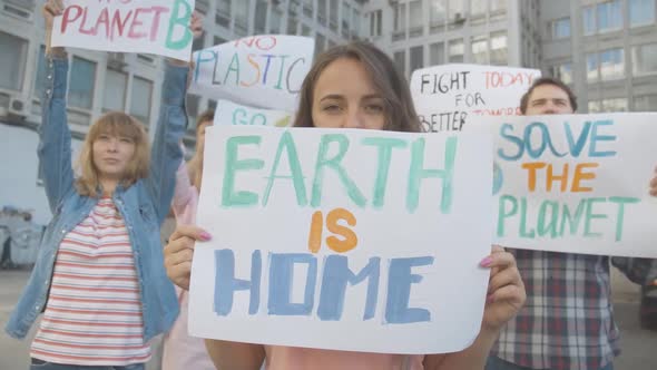 Portrait of Woman Holding Earth Is Home Poster and Looking at Camera. Female Protester Standing