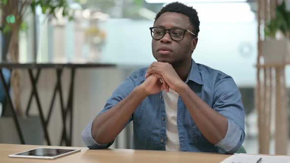 Young African Man Sitting in Modern Office and Thinking