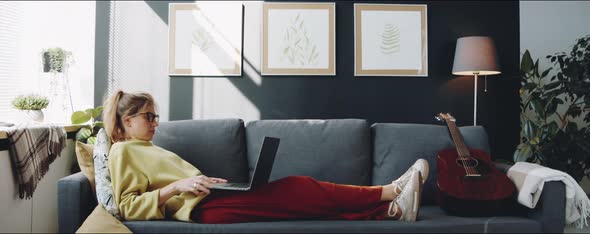 Young Woman Lying on Couch and Using Laptop at Home