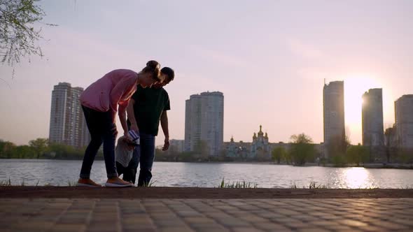 Young Mother and Father Teach the Child to Walk Along the Path