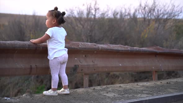 Small South African black girl standing on a low bridge in a winter landscape