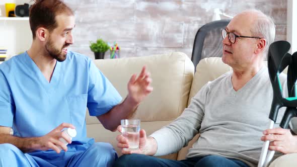 Male Nurse Giving Pills To Retired Man in Nursing Home