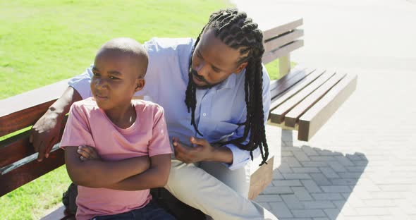 Video of african american father sitting on bench and talking with angry son