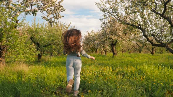 Active Teenager Girl Running Through Blooming Apple Orchard