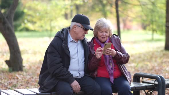 Happy Senior Couple Laughing and Exciting with Something in Smartphone Mobile While Sitting in the