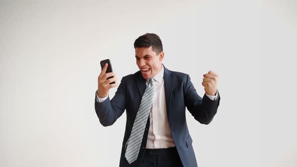 Happy Male Office Worker in Formal Clothes Uses Mobile Phone Rejoices in Victory