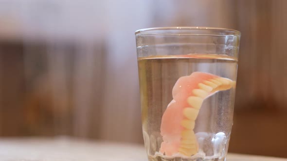 Close-up of a glass of water, a senior citizen takes out false dentures.
