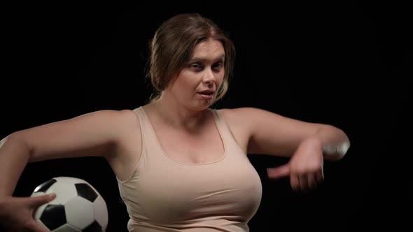 Confident Attractive Plus Size Woman Posing with Soccer Ball at Black Background Gesturing Thumb Up