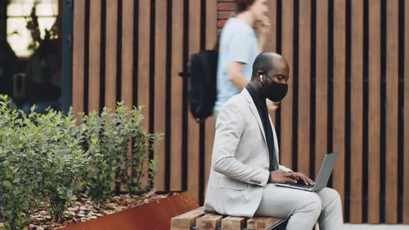 Time Lapse of Black Businessman in Mask Working on Laptop on Street Bench