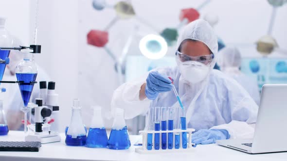 Female Scientist Taking Samples of Blue Liquid From Different Test Tubes Using a Pipette