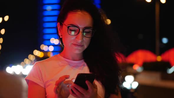 Pretty Woman Stands on the Street in a White T-shirt and Glasses, Makes Online Payments By Credit