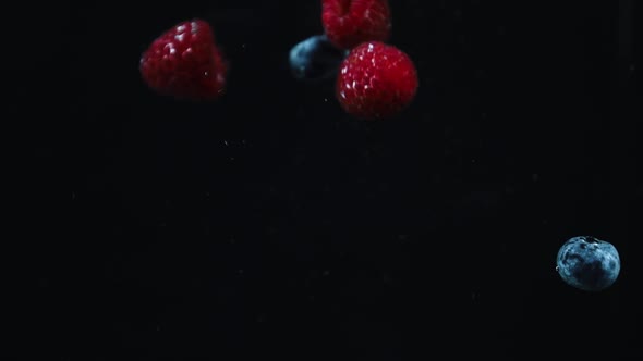 raspberry and blueberries in water black background