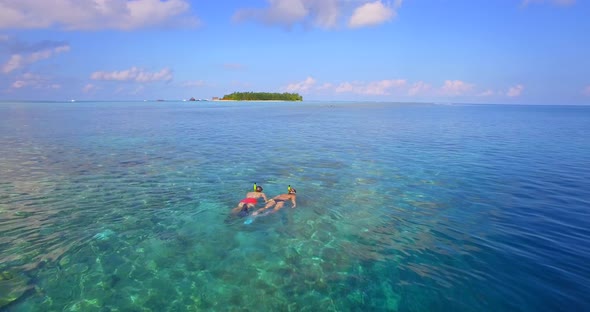 Aerial drone view of a man and woman couple snorkeling over the coral reef of a tropical island