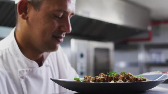 Caucasian male chef garnishing dish and smiling in restaurant kitchen