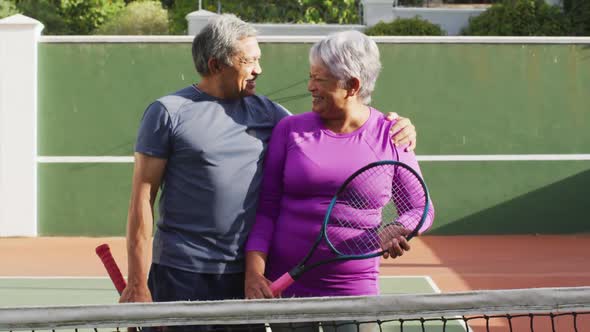 Video of happy biracial senior couple holding rackets on tennis court