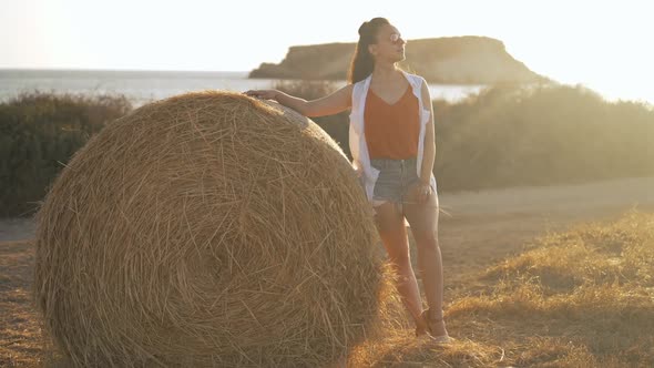 Wide Shot Young Slim Woman Standing in Sunbeam at Yellow Haystack on Field Looking Around