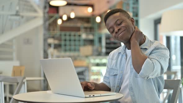 Stressed African Man having Neck Pain in Cafe