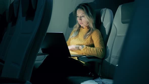A Woman Is Working on a Laptop During Her Night Flight. Female Freelancer Working on Laptop Sitting