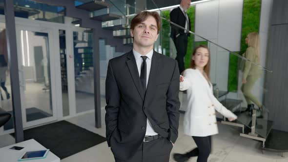 Confident Elegant Handsome Man Posing in Luxurious Office with Colleagues Passing Greeting