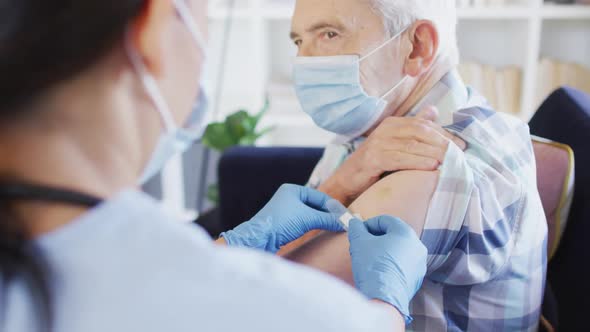 Video of hands of biracial female doctor vaccinating caucasian senior man