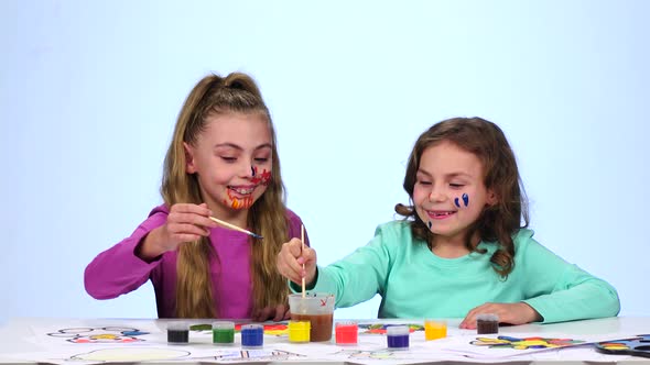 Two Little Sisters Decorate Their Faces with Colorful Colors. Close Up. White Background alt