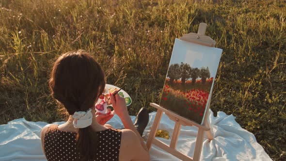 Young girl paints the picture on canvas in the countryside