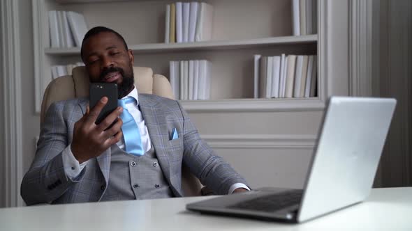 African-American Sleepy Bearded Man in a Gray Suit and Shirt. The Businessman Is in a Bright Office