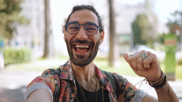 Cheerful curly-haired bearded man in eyeglasses waving hand at the camera and pointing to the side