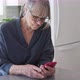 Senior Caucasian woman using smartphone while sitting at kitchen counter - VideoHive Item for Sale