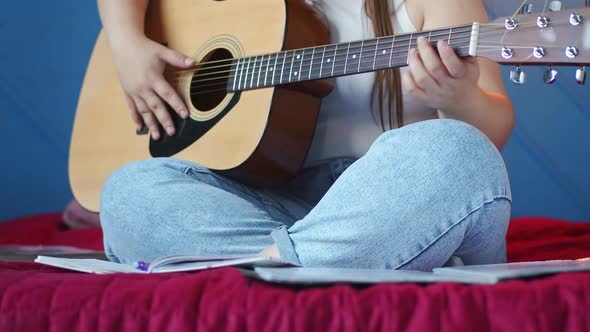 Woman is Sitting on Sofa Playing Guitar and Writing Down Important Things in Notebook Front View